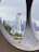 A cityscape featuring a prominent futuristic tower, surrounded by modern skyscrapers and framed by a large circular metal structure. The cloudy sky casts a muted, grayish tone over the urban scene.