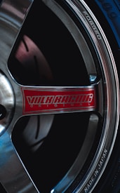 A close-up view of a car wheel, featuring a metallic finish with the words 'FORGED' and 'MADE IN JAPAN' inscribed on the rim. The hub sports a red label with the logo 'VOLK RACING', emphasizing the brand. The image highlights the sleek design and craftsmanship of the wheel.
