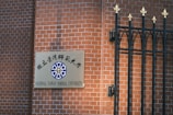 A sign for National Taiwan Normal University is mounted on a red brick wall next to a decorative black metal fence with golden finials.