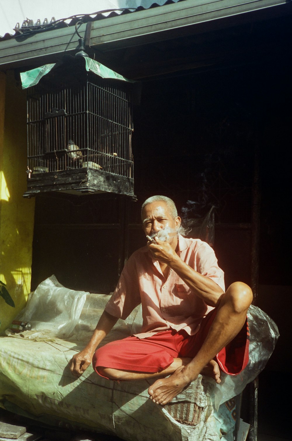 a man sitting on top of a bed next to a bird cage