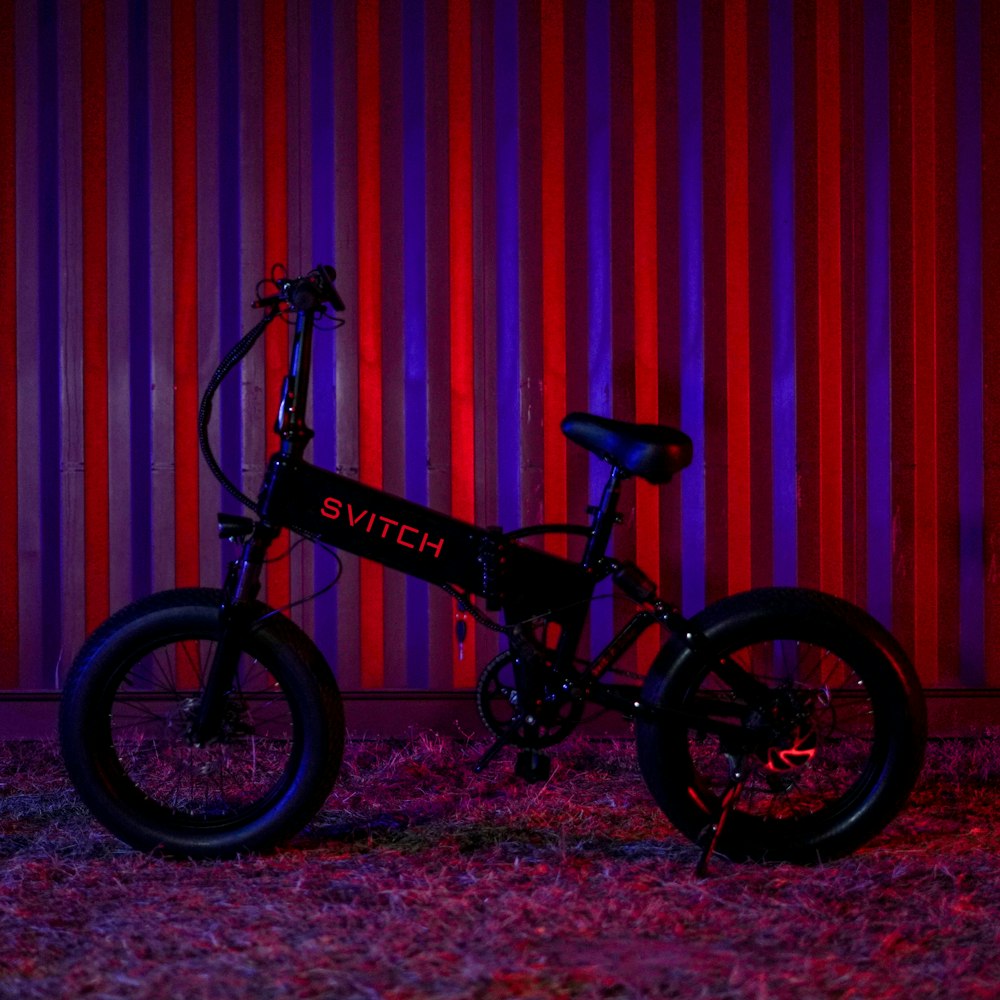 a black bicycle parked in front of a red and purple striped wall