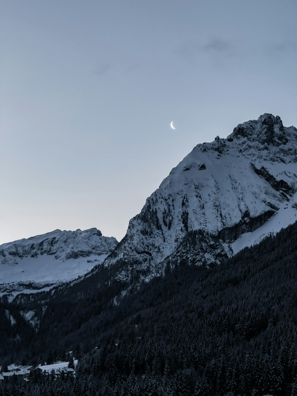 a snowy mountain with a half moon in the sky