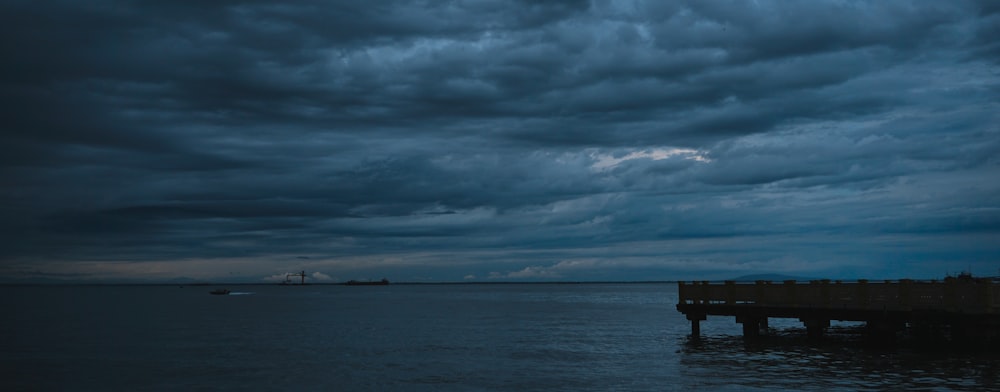 a pier in the middle of a body of water under a cloudy sky