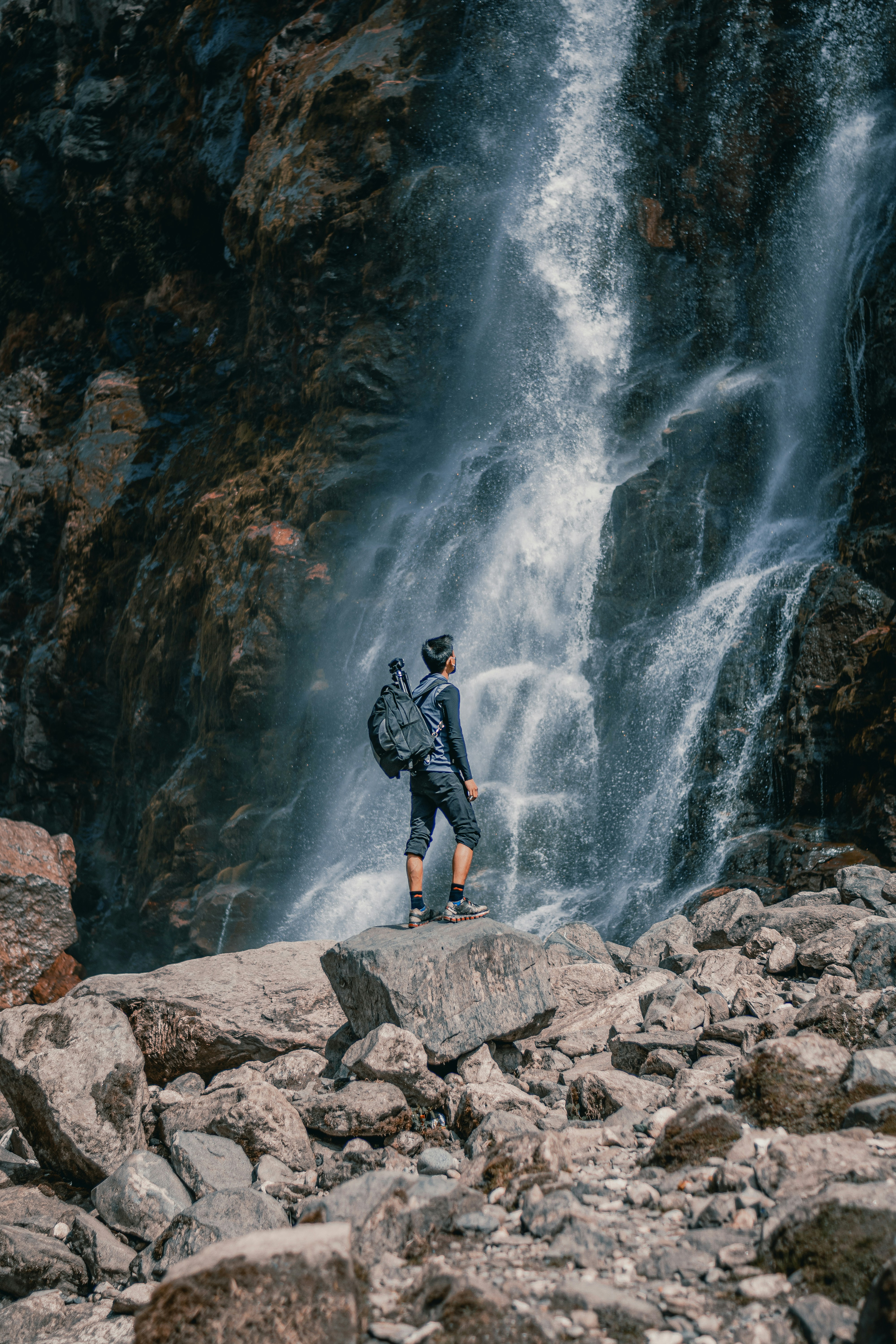a man with a backpack standing on a rock near a waterfall