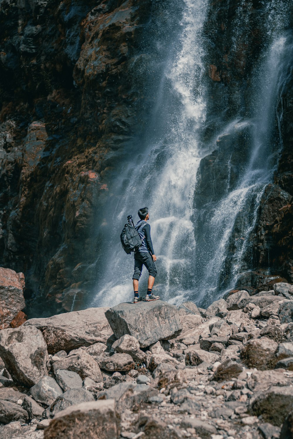 a man with a backpack standing on a rock near a waterfall