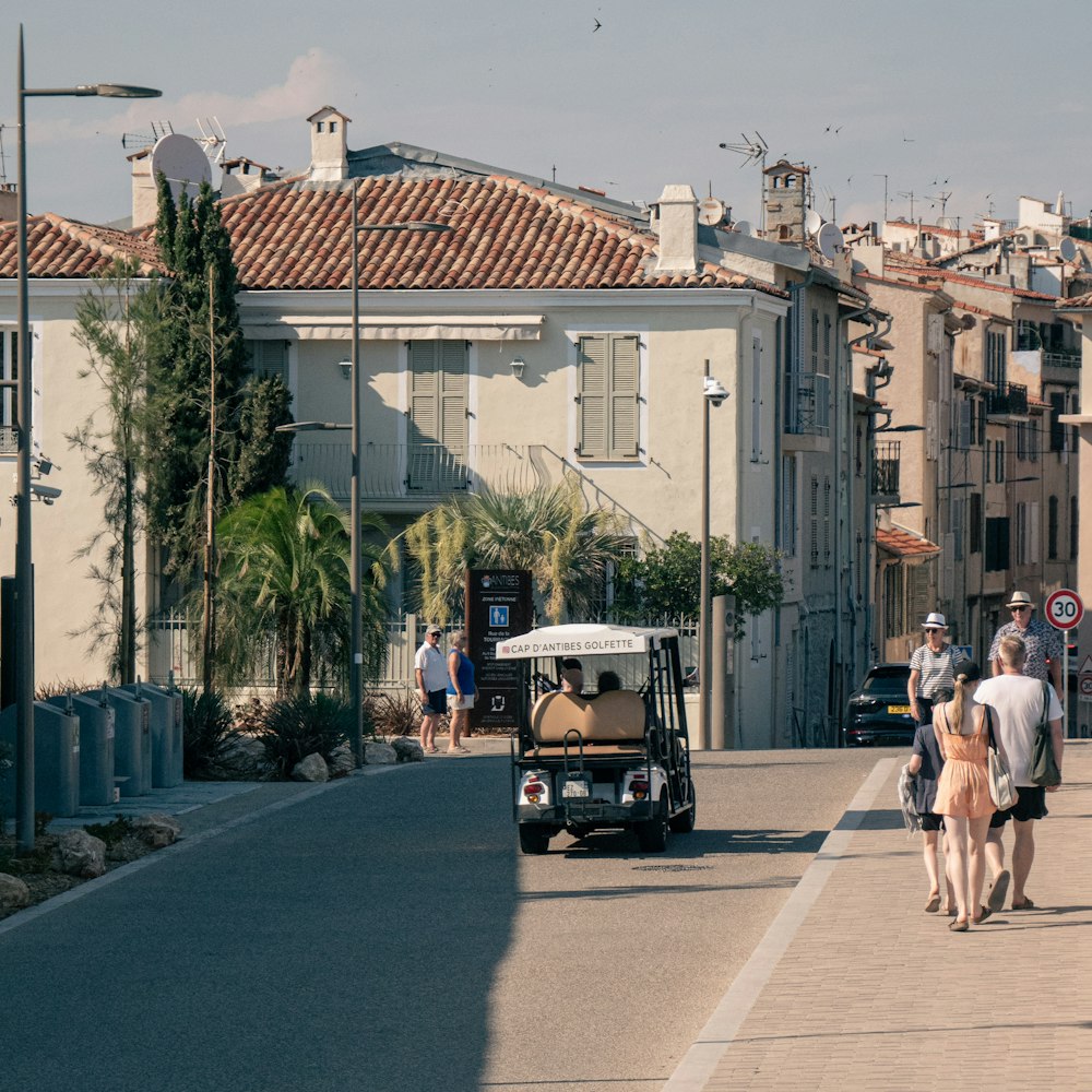 um grupo de pessoas andando por uma rua ao lado de um carrinho de golfe