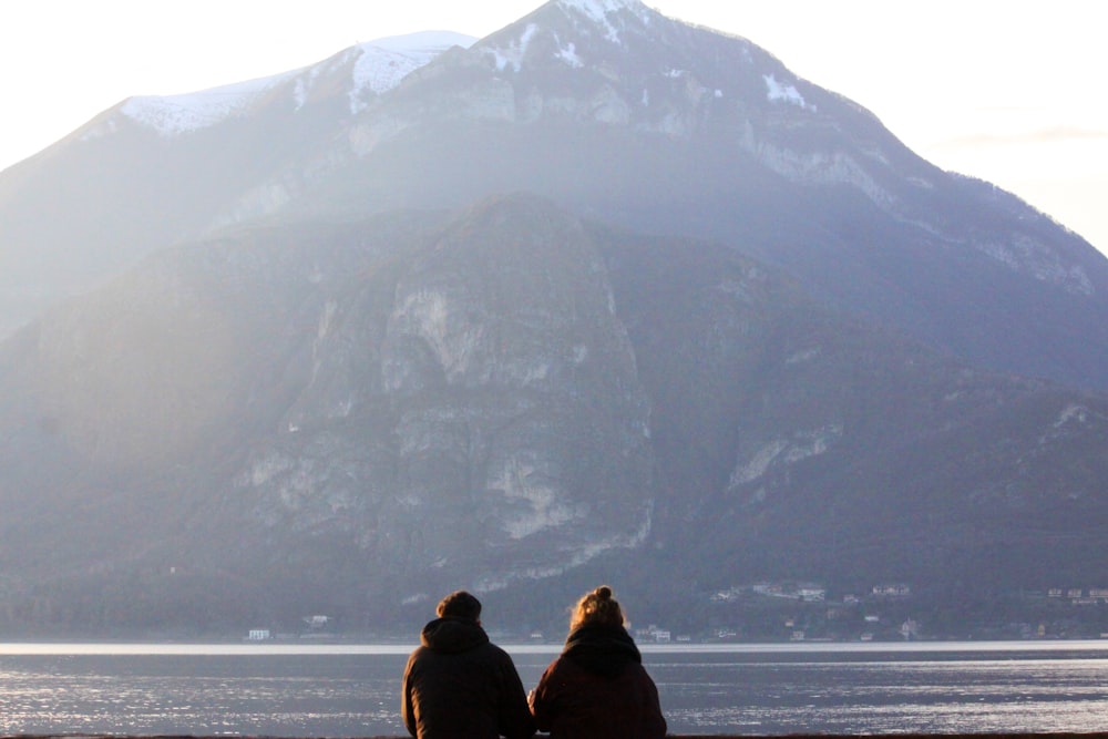two people sitting on a bench looking at a mountain