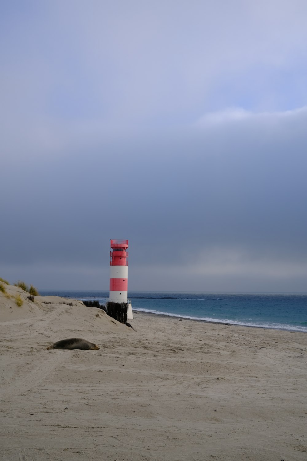 a red and white lighthouse sitting on top of a sandy beach