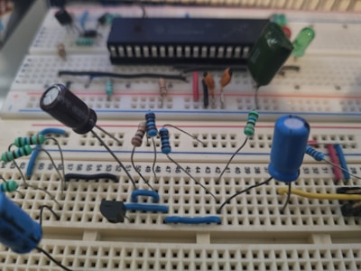 This is a close-up image of an electronic breadboard setup featuring various electronic components. Several resistors with colored bands are arranged neatly across the board, along with capacitors that are identifiable by their canister shapes. An integrated circuit (IC) chip is centrally placed, surrounded by various connecting wires.