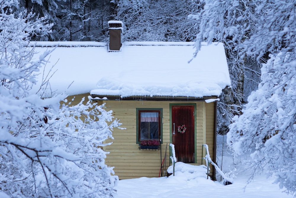 a small yellow house with a red door in the snow
