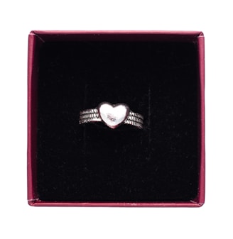 A silver ring with a heart-shaped centerpiece, placed inside a maroon box lined with a black, velvety material.