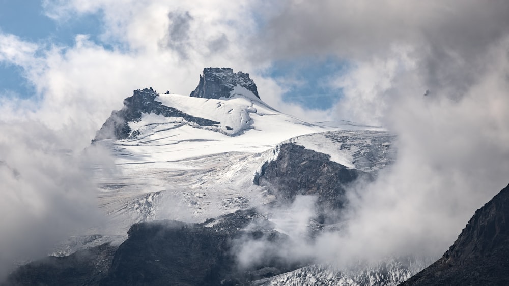 a mountain covered in snow and clouds under a blue sky