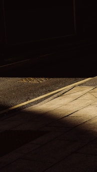 A grainy black-and-white photo of a deserted urban street corner, sharp shadows cutting across concrete slabs.