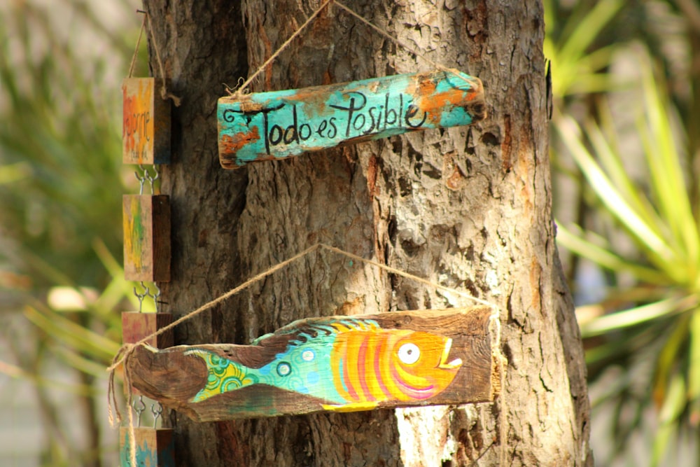 a wooden sign hanging from a tree with a fish painted on it