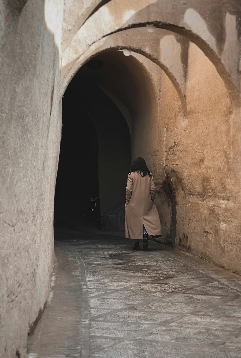 a woman in a trench coat walking through a tunnel