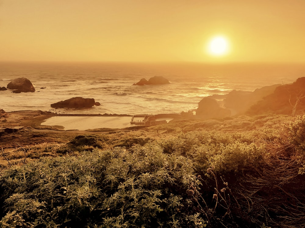 the sun is setting over the ocean with rocks