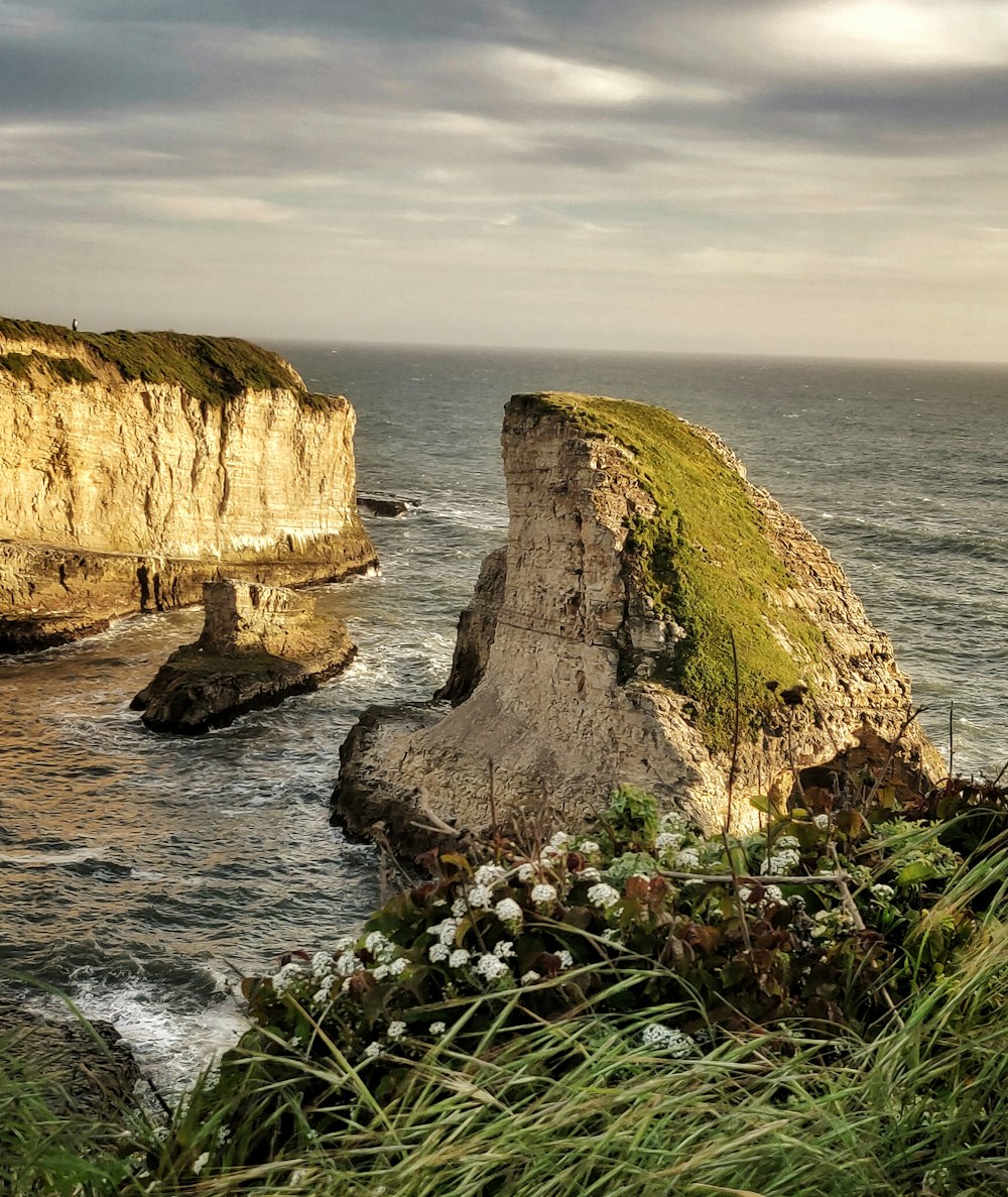 Una grande roccia seduta sulla cima di una collina verde lussureggiante vicino all'oceano