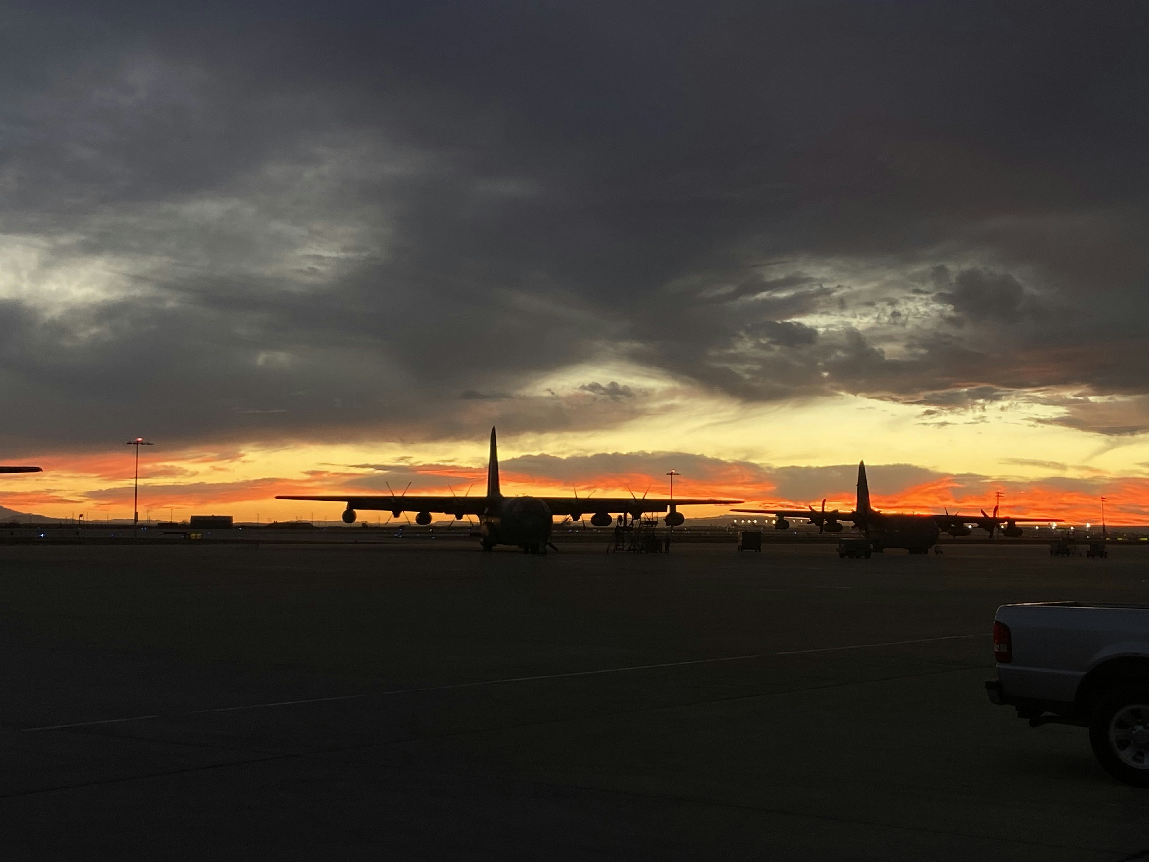 Cargo aircraft on runway at dawn, bright orange sky, industrial airport ground operations, dark aircraft silhouette against warm light