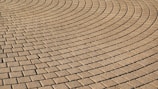 Interlocking brick pavement forms an intricate pattern of curved lines. The bricks are uniformly arranged, creating a textured and visually captivating surface.