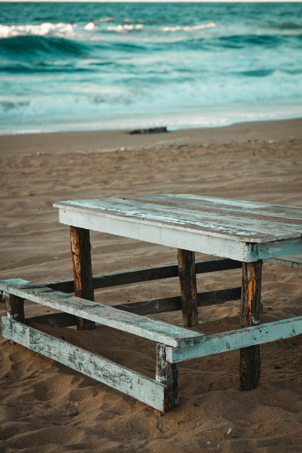 a wooden picnic table sitting on top of a sandy beach