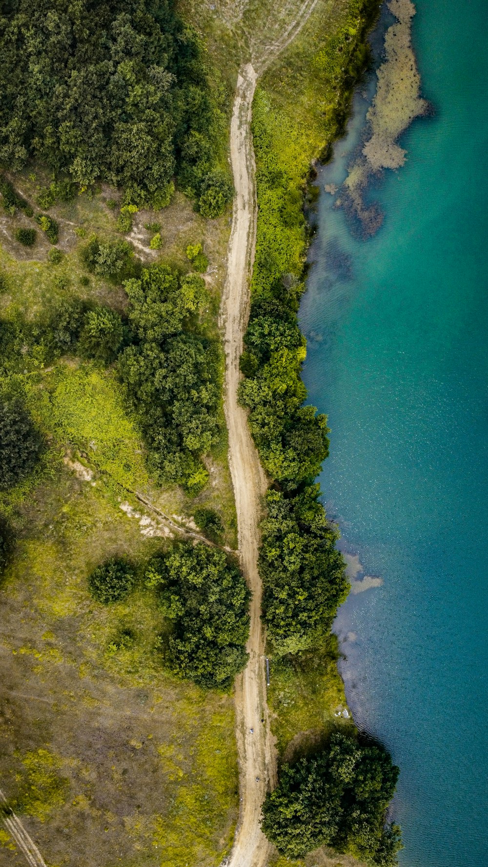 an aerial view of a dirt road next to a body of water