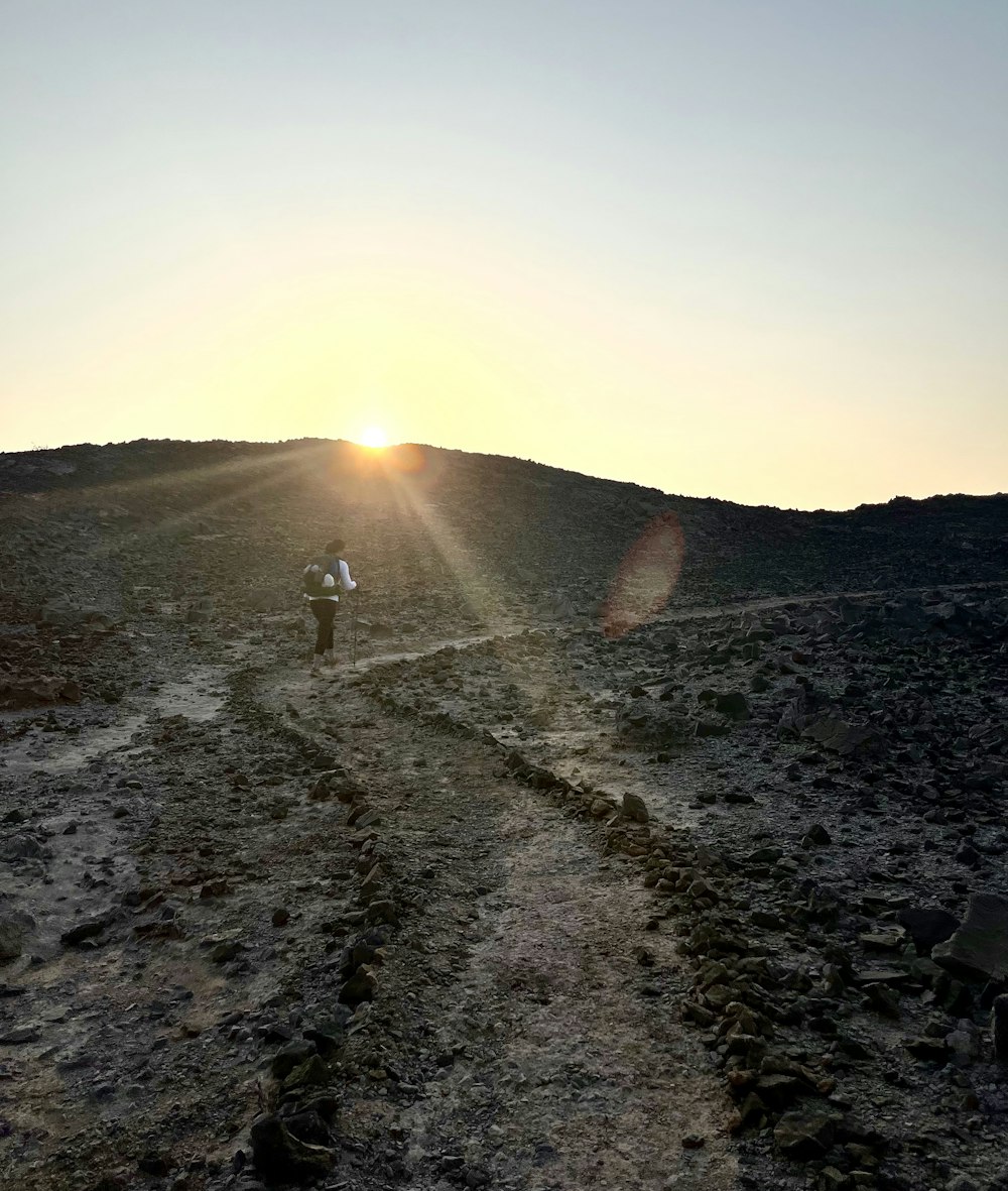 two people walking up a dirt path at sunset