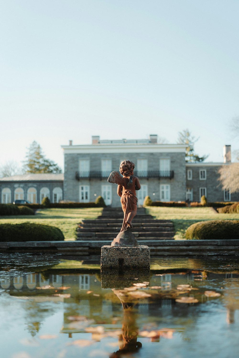 a statue of a woman standing on a rock in front of a pond