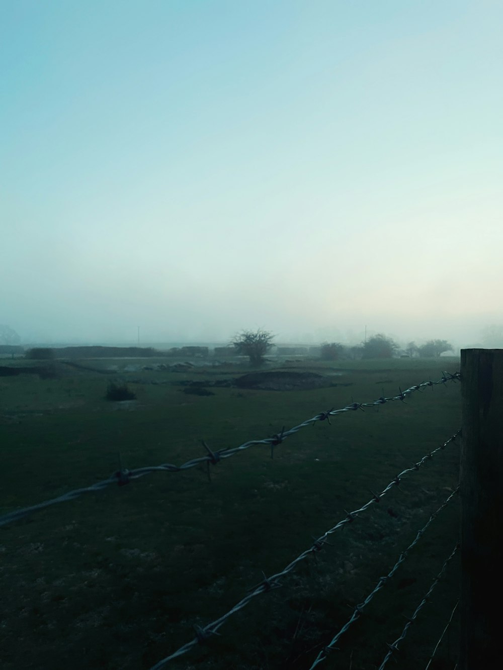 a foggy field with a fence in the foreground