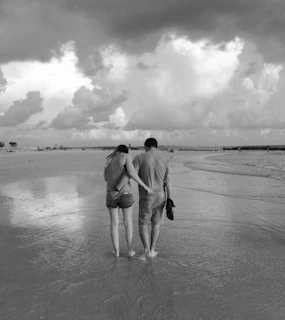 A warm, cinematic capture of a couple walking barefoot along a sandy shore.