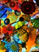 A vibrant and colorful glass sculpture consisting of various intricate patterns and shapes. The artwork features a harmonious blend of colors, including vivid blues, reds, oranges, yellows, and greens, creating a dynamic and mesmerizing visual experience. The glass pieces are layered and interwoven, each exhibiting unique textures and designs.