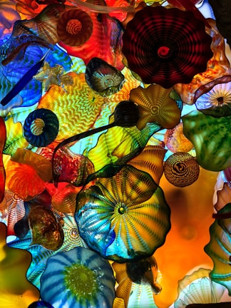 A vibrant and colorful glass sculpture consisting of various intricate patterns and shapes. The artwork features a harmonious blend of colors, including vivid blues, reds, oranges, yellows, and greens, creating a dynamic and mesmerizing visual experience. The glass pieces are layered and interwoven, each exhibiting unique textures and designs.