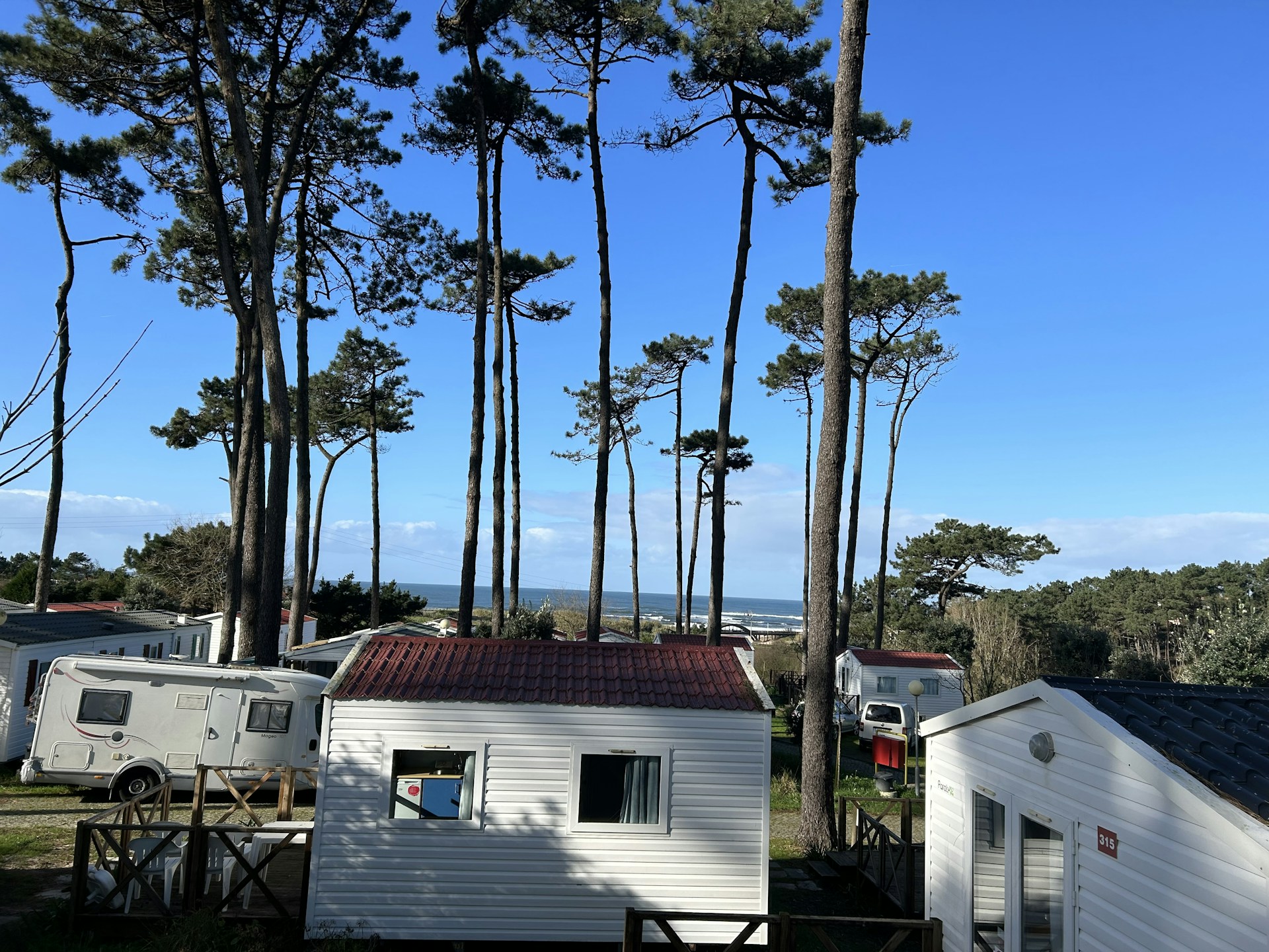 A cozy mobile home nestled among pine trees near a sparkling seaside with a vibrant water park in the background.
