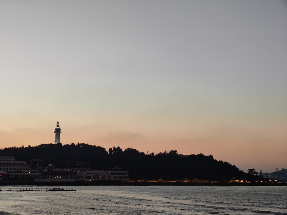 a body of water with a light house on a hill in the background