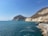 A scenic view of a turquoise coastline with a car parked on a cliffside overlooking the sea.