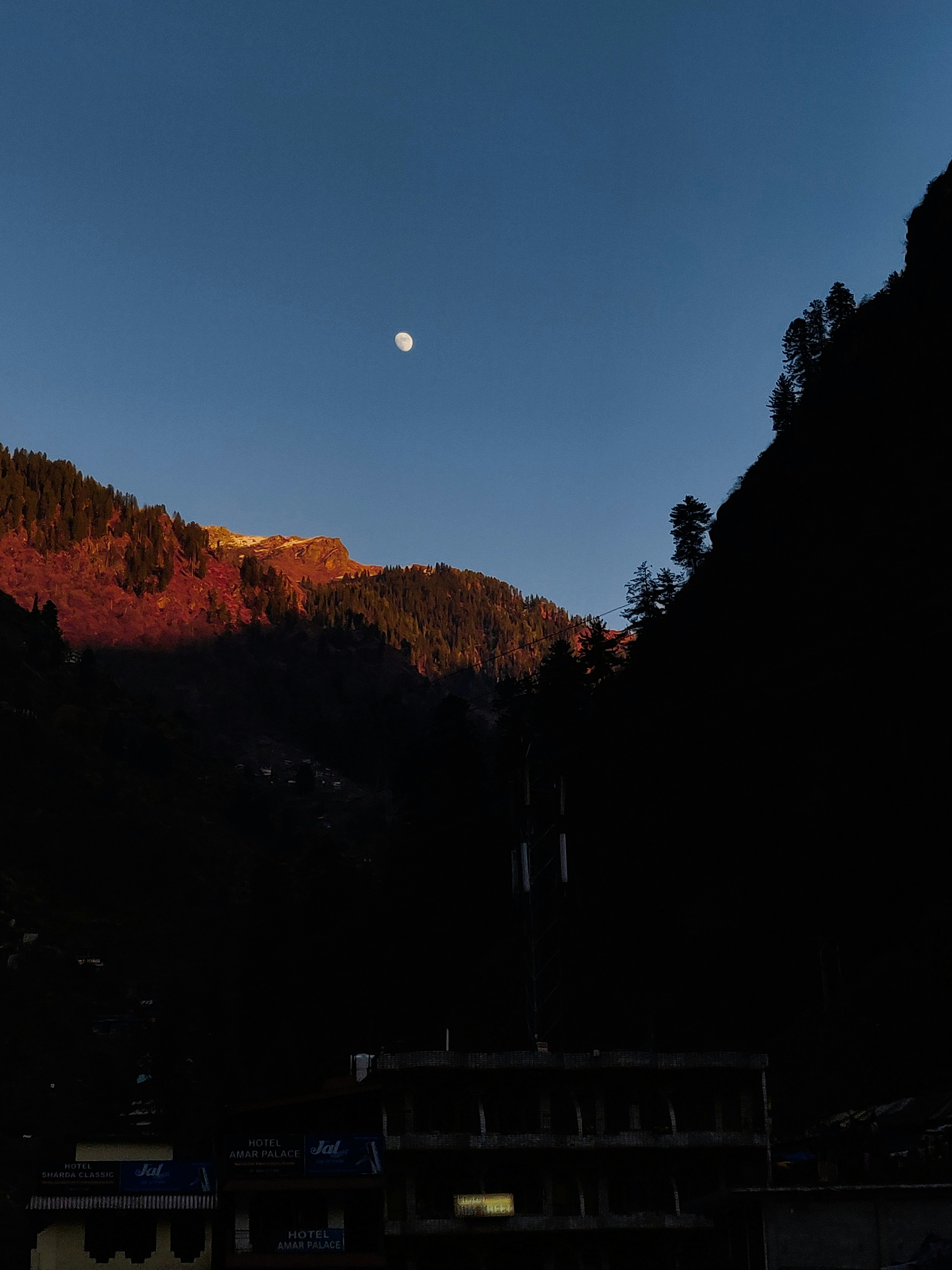 the moon is setting over a mountain range