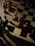 A chessboard is partially visible, featuring several chess pieces arranged on it. The pieces are mostly pawns, with a mix of light and dark colors. The board is set on a wooden surface, and the lighting creates strong contrasts, with shadows cast across the board and pieces.