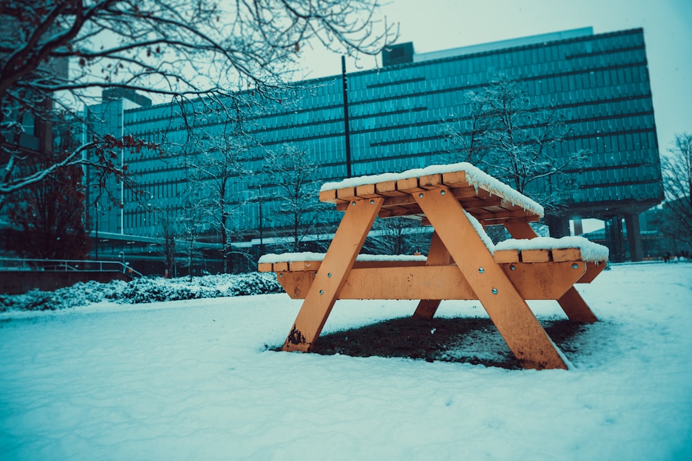 a wooden picnic table covered in snow in front of a building