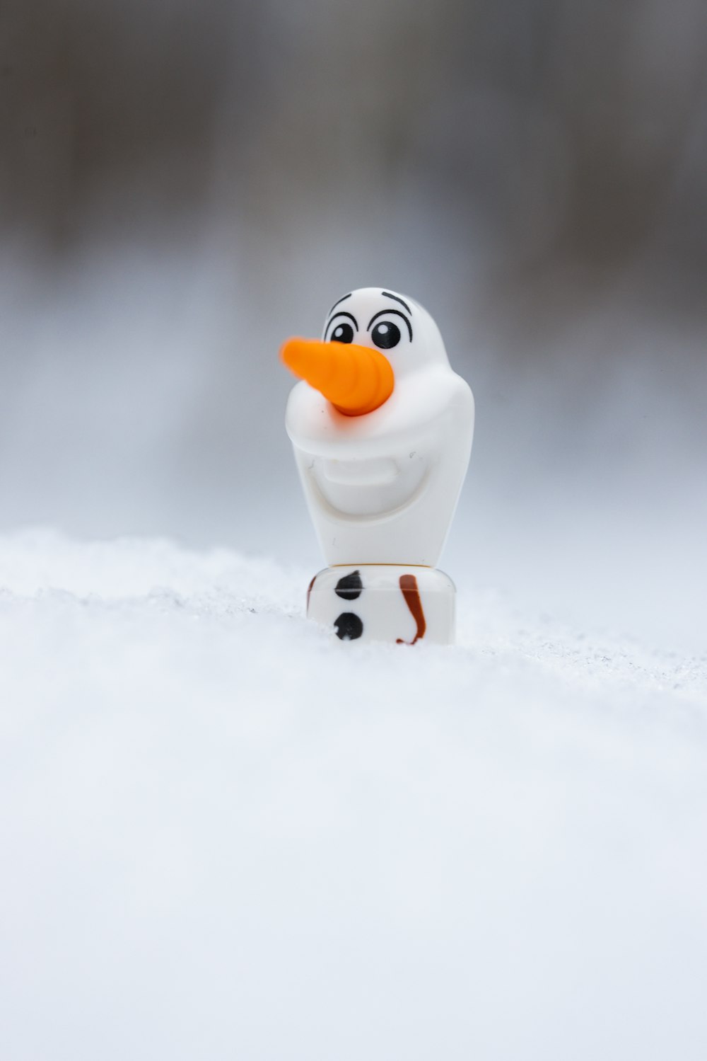 a toy snowman with an orange nose standing in the snow