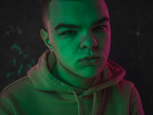 A moody, industrial shot of a model wearing a black hoodie with neon green accents under harsh shadows.