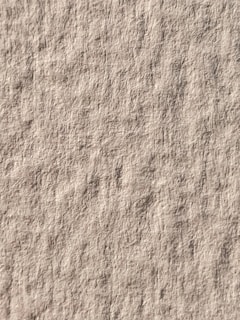 A textured surface with a uniform pattern similar to a rough canvas or paper. The image is dominated by a neutral, earthy tone.