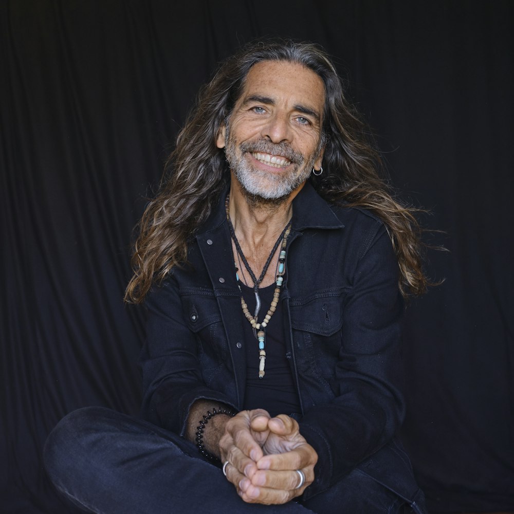 a man with long hair sitting on the ground