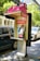 A public payphone booth with a pink canopy displaying a Telstra logo and offering free Wi-Fi is situated on a city street. Nearby, parked cars and trees are visible, suggesting an urban environment. The booth features a metallic payphone unit with a keypad and display.