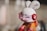 A toy figure resembling a rabbit with an exaggerated cartoon style, featuring white fur, large ears, and a pink visor covering its eyes. The figure is adorned with red earmuffs with a peace sign symbol and wears an orange and red outfit.