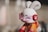 A toy figure resembling a rabbit with an exaggerated cartoon style, featuring white fur, large ears, and a pink visor covering its eyes. The figure is adorned with red earmuffs with a peace sign symbol and wears an orange and red outfit.