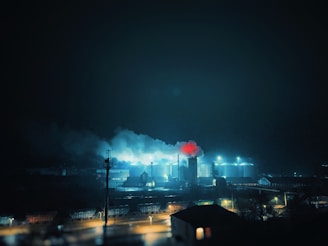 A large industrial refinery complex at dusk with smoke stacks and glowing lights.