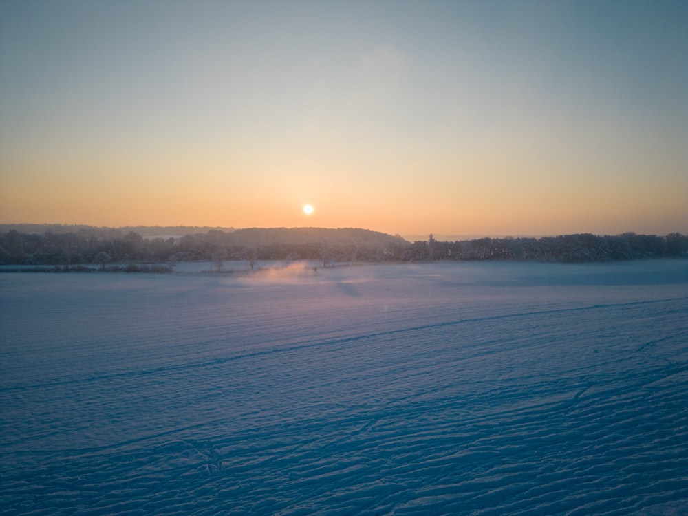 the sun is setting over a snowy field