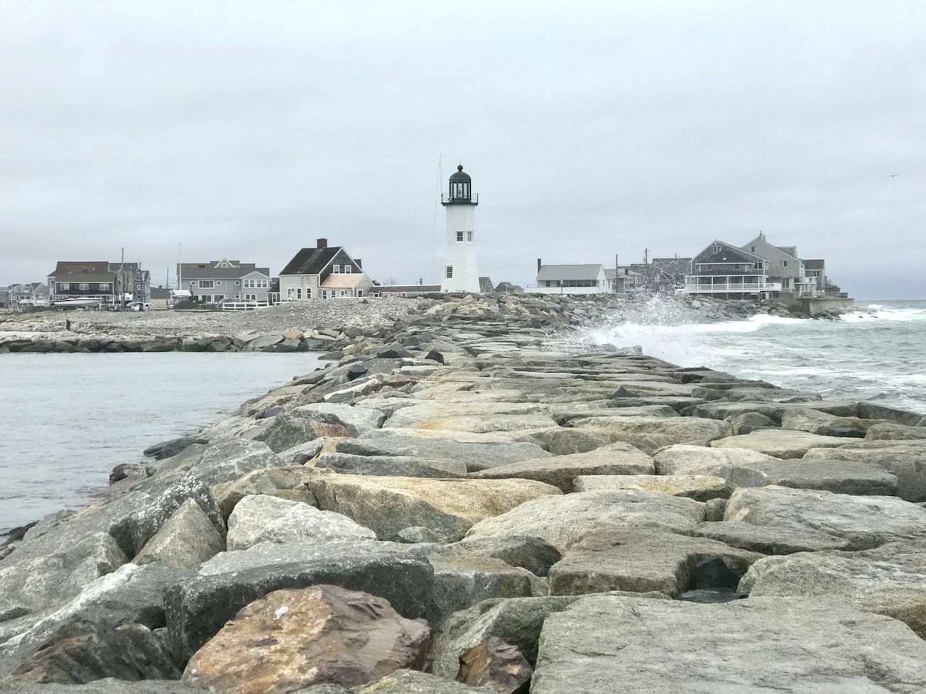 Olas rompen junto a un faro en la costa rocosa de Scituate, Massachusetts