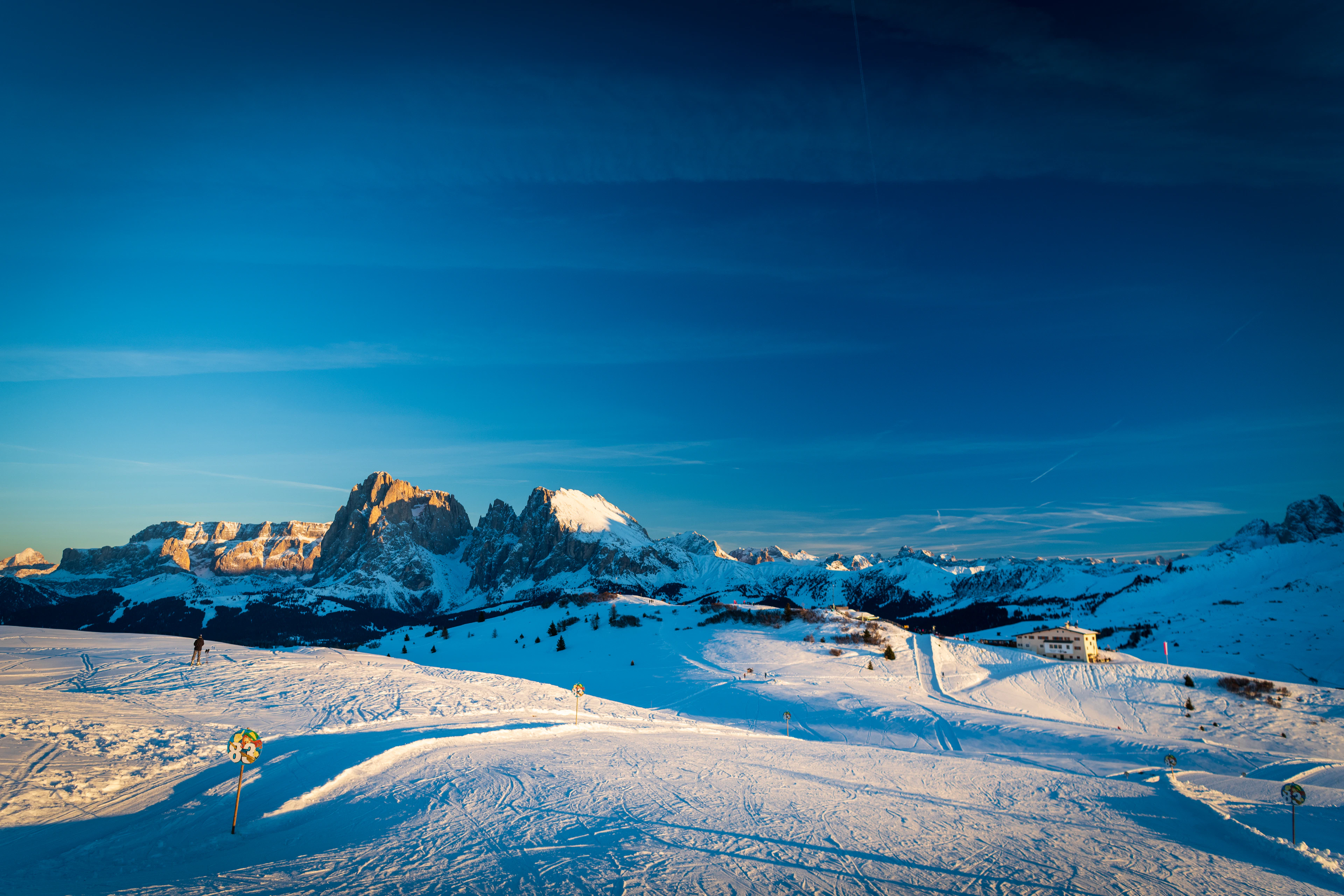 Ski tracks cross the wide, gentle slopes of the Seiser Alm at dusk, with Dolomite rock peaks lit by the last sun