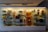 A display case filled with a variety of eclectic objects, including a mannequin, dolls, books, bottles, hats, masks, and figurines. The arrangement is colorful and visually interesting with a mix of modern and vintage items.