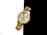 A gold wristwatch with a metallic band and a round face featuring a crystal-studded bezel is positioned against a stark black and white background. The watch face shows three sub-dials and has a sophisticated, luxurious appearance with gold detailing.